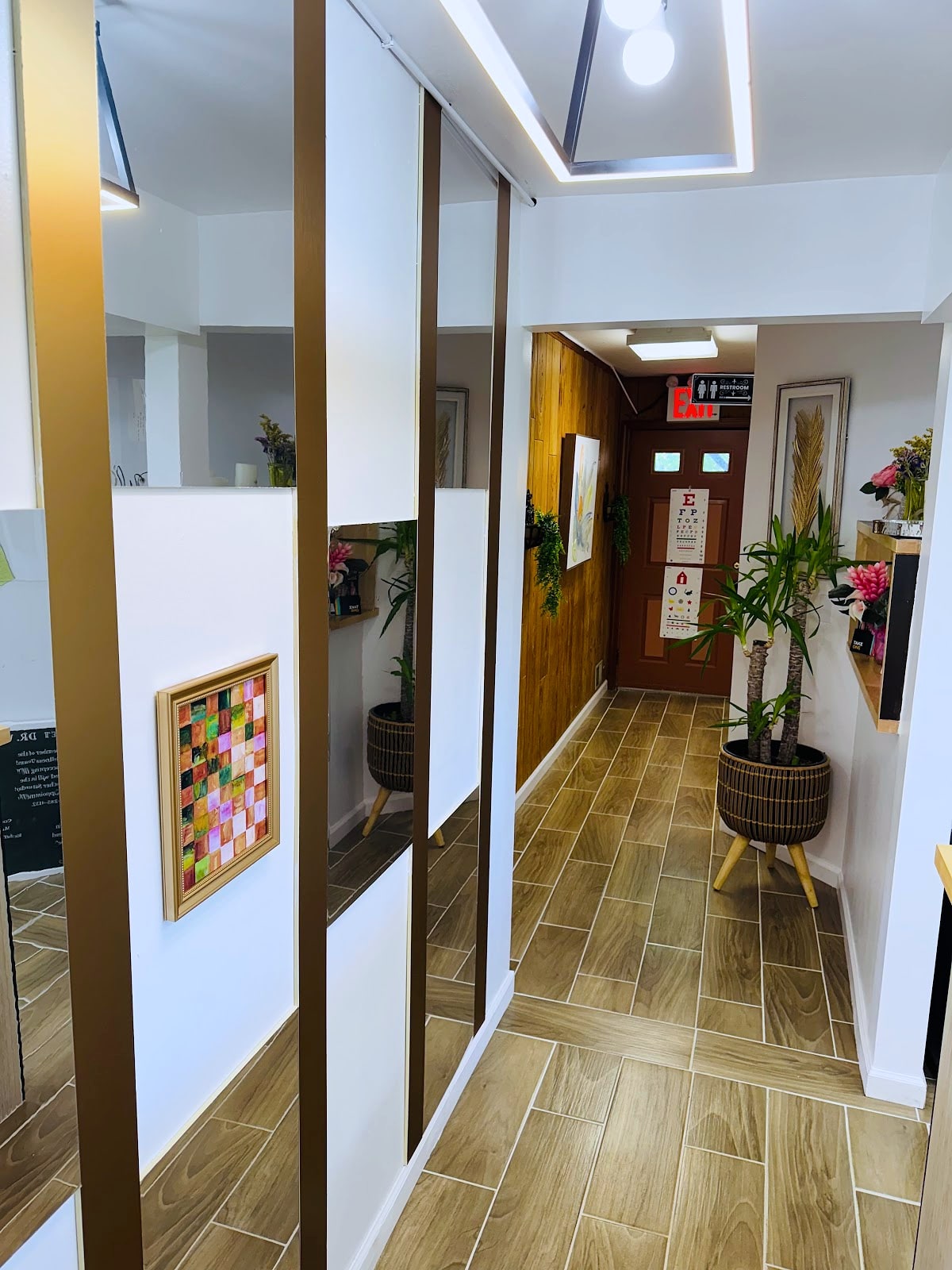 Clinic hallway with mirrored panels, wood flooring, potted plants and an eye chart